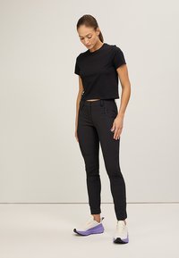 Svart kortärmad t-shirt i kombination med åtsittande svarta byxor med blixtlåsfickor. Modellen har på sig ljusa sneakers med lila accenter.