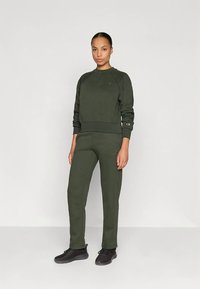 Sweatshirt desportivo verde escuro e calças combinando feitas de tecido macio. Apresenta punhos e cós canelados, com detalhes de logótipo em ambas as peças.