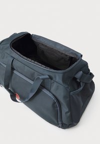 Mørkegrå duffelbag lavet af tekstureret nylon. Har en rummelig åbning, robuste håndtag og en sidelomme med lynlås. Foret er sort.