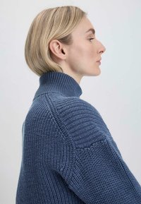 Gebreide coltrui in donkerblauw. Beschikt over een ribbeltextuur, verlaagde schouders en een dikke kraag, wat zorgt voor een comfortabele en gestructureerde uitstraling.