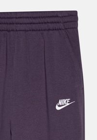 Violet sportinės kelnės su minkšta tekstūra, turinčios elastinį diržą ir baltą Nike logotipą dešinėje šlaunyje.