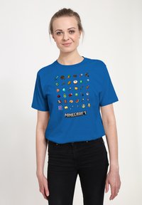 Modrá bavlněná trička s mřížkou ikon inspirovaných Minecraftem v různých barvách, s nápisem "MINECRAFT" vytištěným ve spodní části.