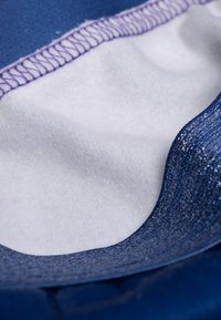 Tessuto blu con una texture liscia e cuciture viola nella parte superiore. Tessuto bianco morbido sottostante, che mostra un design a strati.