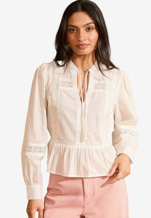 Blusa bianca con maniche lunghe, design plissettato, dettagli in pizzo sulle spalle e vita a peplo. Tessuto texturizzato con sottili motivi a pois.
