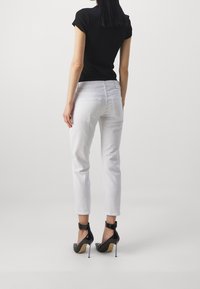 Musta tiukka toppi, valkoiset lyhyet farkut ja mustat kiiltävät korkokengät. Takaviisto näyttää farkkujen takataskut ja kengissä olevat nilkkahihnat.