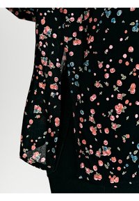 Svart blus med blommönster i rosa och blåa blommor. Tillverkad av lätt tyg, den har en liten sidoklyvning för ökad bekvämlighet.