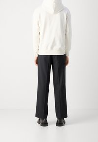 Vit huva sweatshirt och svarta vida byxor. Sweatshirten är mjuk, med ribbat fåll. Byxorna har en slät yta och veck. Svarta skor syns.