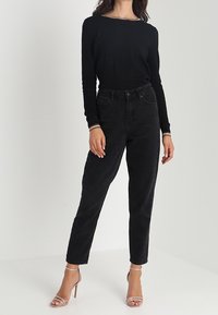 Czarna bluzka z długim rękawem i dekoltem typu łódka, zestawiona z wysokim stanem czarnych jeansów oraz beżowymi sandałami na cienkich paskach. Prosty, dopasowany krój, gładka faktura.