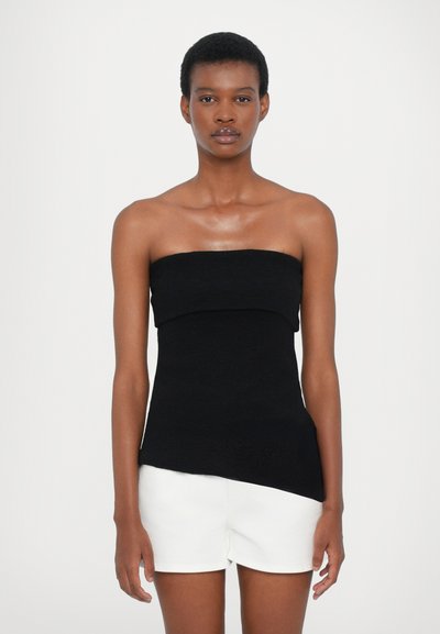 Top noir sans manches avec un décolleté arrondi et un ourlet asymétrique. Le tissu a une texture douce, associé à un short blanc.