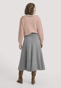 Heller rosa gerippter Pullover mit Rundhalsausschnitt und grauem schwingendem Rock. Das Model trägt knielange braune Stiefel. Weiche Texturen und lässige Passform.