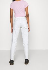 Pantaloni in denim bianco con vestibilità rilassata, due tasche posteriori e passanti per cintura. Abbinati a una maglietta rosa a maniche corte. Stivaletti neri alla caviglia in vista.