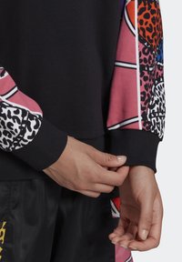 Zwarte sweatshirt met gestreepte roze en witte mouwen, versierd met luipaard- en abstracte ontwerpen. Textuur manchetjes maken de look compleet.