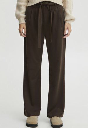 Brown, high-waisted wide-leg pants with a tie waist detail and pleats; made of a soft, smooth fabric; paired with beige footwear.