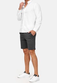 Chemise boutonnière en lin blanc, shorts gris et baskets blanches. La chemise a un col et des manches longues ; les shorts sont à mi-genoux avec des poches.