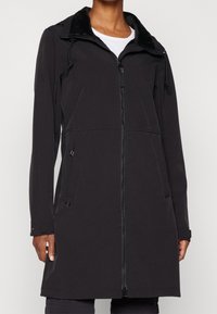 Black softshell jacket with a zippered front, long sleeves, and a faux fur-lined collar. Features side pockets and adjustable drawstrings.