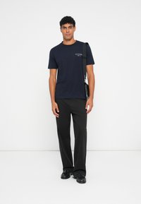 Navy blue cotton t-shirt with short sleeves and a small logo on the chest, paired with black trousers and black shoes.