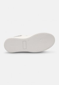 White sneaker sole featuring a herringbone pattern, circular and rectangular treads, and a smooth texture with a subtle logo detail.