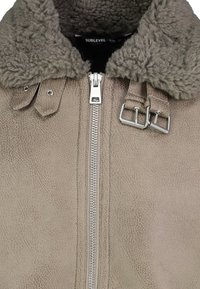 Leren jack in taupe met een gestructureerde afwerking, voorzien van een schapenvachtkraag, zilveren rits en verstelbare banddetails op de schouders.