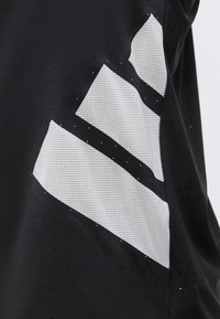 Tissu noir avec de petites perforations présentant trois grandes bandes diagonales blanches texturées.