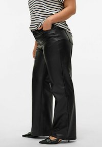 Pantaloni neri in eco-pelle a gamba larga con una texture liscia, due tasche laterali e vita aderente. Abbinati a una camicia a righe e scarpe a punta.