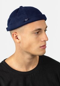 Gorro de algodón azul marino con un borde vuelta, que presenta una pequeña etiqueta de marca. El gorro tiene una textura lisa y un diseño ajustado.