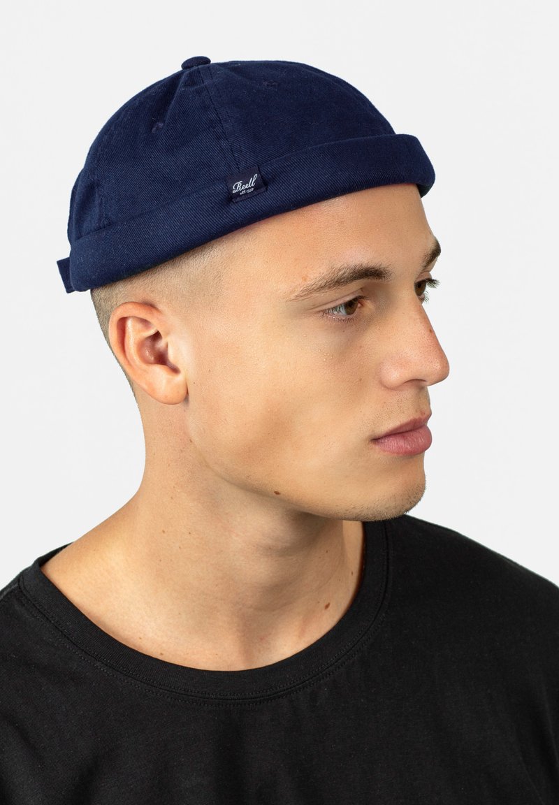 Gorro de algodón azul marino con un borde vuelta, que presenta una pequeña etiqueta de marca. El gorro tiene una textura lisa y un diseño ajustado.