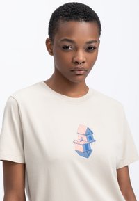 Beige katoenen t-shirt met een grafisch ontwerp van een twee-verdiepingen huis in roze en blauw met kleine accenten. Zachte stof, standaard pasvorm.