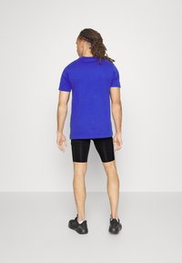 Blaues T-Shirt mit kurzen Ärmeln, aus Baumwolle, in taillierter Passform, kombiniert mit schwarzen Radsportshorts und schwarzen Sportschuhen. Einfach und funktional.