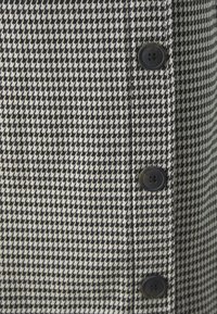 Črnobela tkanina z vzorcem houndstooth z gladko teksturo, ki ima ob vertikalnem šivu štiri črne gumbe.