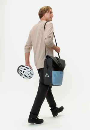 Borsa a tracolla nera con un pannello azzurro chiaro, tracolla regolabile e parte superiore chiusa. Un casco da bicicletta bianco è tenuto nell'altra mano.