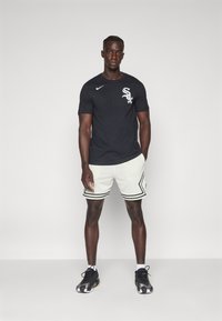 Camiseta negra de Nike de manga corta con logo blanco, combinada con pantalones cortos blancos perforados con acentos negros, y zapatillas deportivas negras.