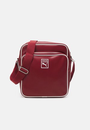 Rød crossbody taske med hvide kanter, justerbar rem, frontlynlåslomme og "Vogue Puma" logo på frontpanelet.