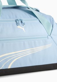 Jasnoniebieska torba podróżna wykonana z trwałej tkaniny, z przednią kieszenią na suwak, beżowym paskowanym wzorem i ciemną czarną podstawą. Logo widoczne.