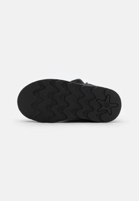 Semelle de chaussure en caoutchouc noir texturé avec des motifs en vagues. Présente un logo central en forme d'étoile et un bord lisse pour une adhérence et une durabilité optimales.