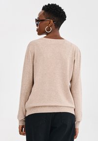 Jasnobrązowy sweter dzianinowy o luźnym kroju z prążkowanymi mankietami. Tył ma szeroki dekolt oraz subtelna tekstura, zestawiony z czarnymi spodniami.