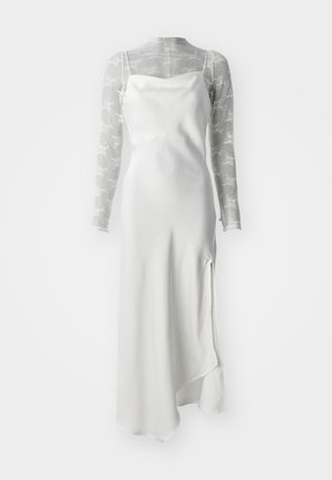 Bílá saténová spodnička s vysokým rozparkem, vrstvená přes průhledný šedý síťový top s dlouhým rukávem, který má bílé květinové vzory.