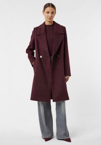 Burgundy wool coat with a double-breasted design, large lapels, and side pockets; paired with wide-leg gray jeans and pointy burgundy shoes.