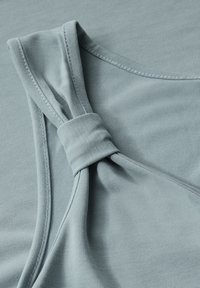 Ljusblå tyglinne med en knuten detalj på axelremmen, med en slät textur och rena sömmar längs kanterna.