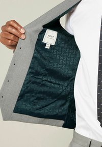 Grey suit jacket with a patterned dark teal lining. Label reads "NEXT TAILORING" with size details. Features black buttons and tailored fit.