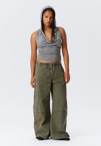 Gray sleeveless top with hood, paired with loose-fitting olive green pants. The fabric appears soft, with visible seams across the pants.
