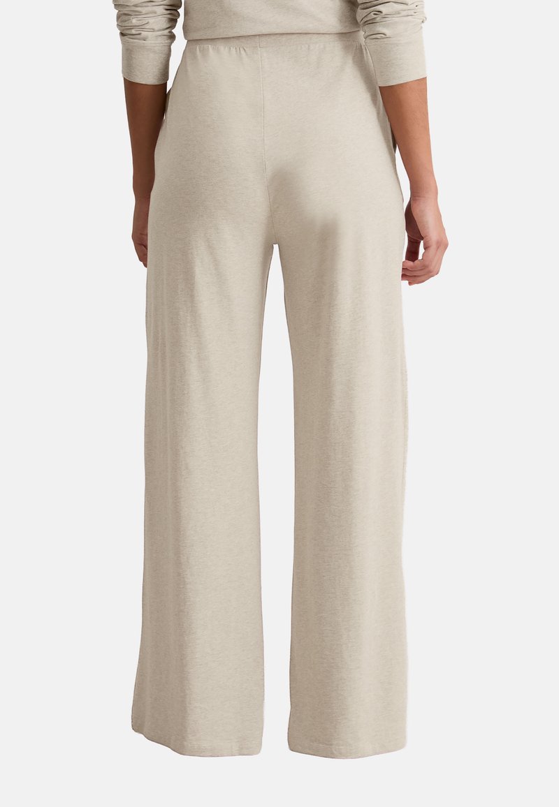 Persona vistiendo pantalones anchos beige mostrada de espaldas con una blusa de manga larga a juego sobre un fondo liso.