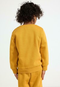 Gelbes Baumwoll-Sweatshirt mit Rundhalsausschnitt, gerippten Bündchen und Saum, von hinten betrachtet. Das passende untere Kleidungsstück ist teilweise sichtbar.