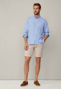Camisa de botão azul claro com detalhes em xadrez, mangas enroladas, calções bege e sapatos slip-on castanhos. Design simples e ajuste casual.