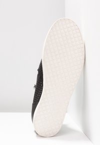 Zapato negro perforado con una suela blanca texturizada. Presenta un zipper lateral y un upper de cuero suave. Vista en ángulo que muestra la textura de la suela.