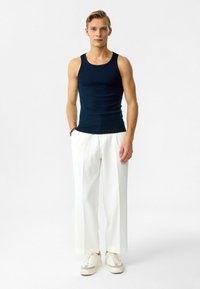 Marineblauw geribd tanktop in combinatie met witte, wijdvallende broeken en crèmekleurige sneakers, met een ontspannen pasvorm en subtiele textuurelementen.