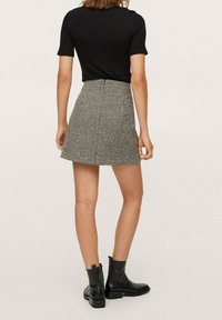 Zwarte korte mouwen top gecombineerd met een flared mini rok met een houndstooth patroon. Zwarte enkellaarsjes maken de outfit af.