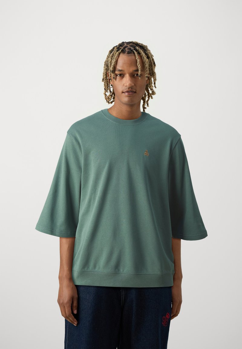 Grøn oversized T-shirt med korte ærmer, rund halsudskæring, tekstureret stof og små broderede detaljer på brystet. Bærer den med mørke denim.