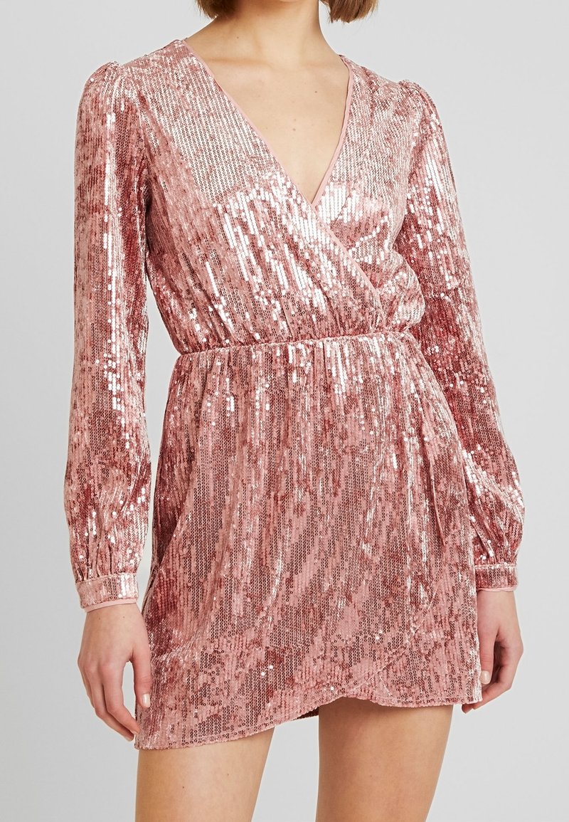 Robe courte en sequins roses avec décolleté en V et manches longues. Elle présente une taille cintrée et un bas en plusieurs couches avec un ourlet légèrement évasé.