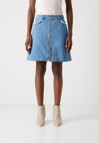 Lys blå denimskjørt med glidelås foran, slitte lommekanter og svingende kant. Bært med beige ankelstøvler og en tettsittende topp.