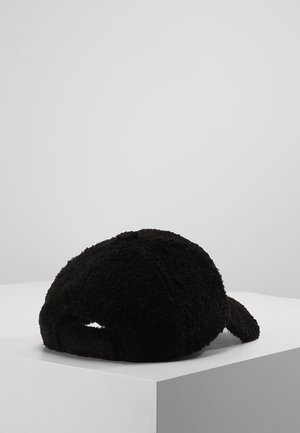 Casquette de baseball en polaire noire et texturée reposant sur une surface blanche avec un fond gris uni.
